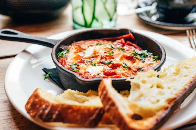 Freshly made shakshuka with spiced tomato, red pepper, feta, egg, coriander and pieces of homemade sourdough, served in iron pan, healthy breakfast