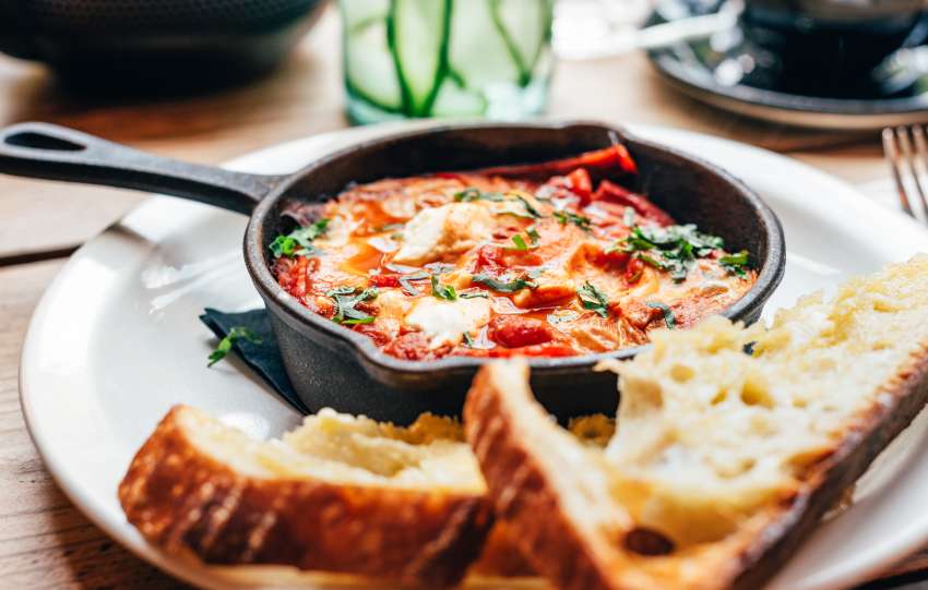 Freshly made shakshuka with spiced tomato, red pepper, feta, egg, coriander and pieces of homemade sourdough, served in iron pan, healthy breakfast